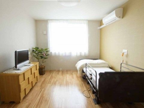 日当たりの良いワンルームの居室である。デザイン性のある収納棚の上には白いレースが敷かれており、テレビが設置されている。