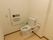 トイレの便座の周りにはＬ字型と可動式の手すりが設置されている。壁には緊急時にスタッフを呼び出せるボタンがある。