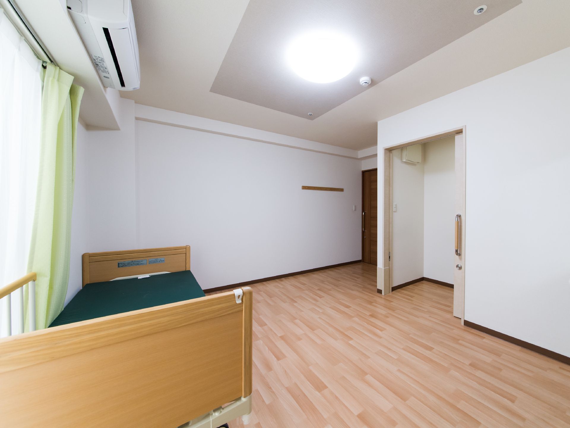 天井には明るいシーリングライトとエアコンが設置されている。フローリングの部屋で、リクライニングベッドがある。