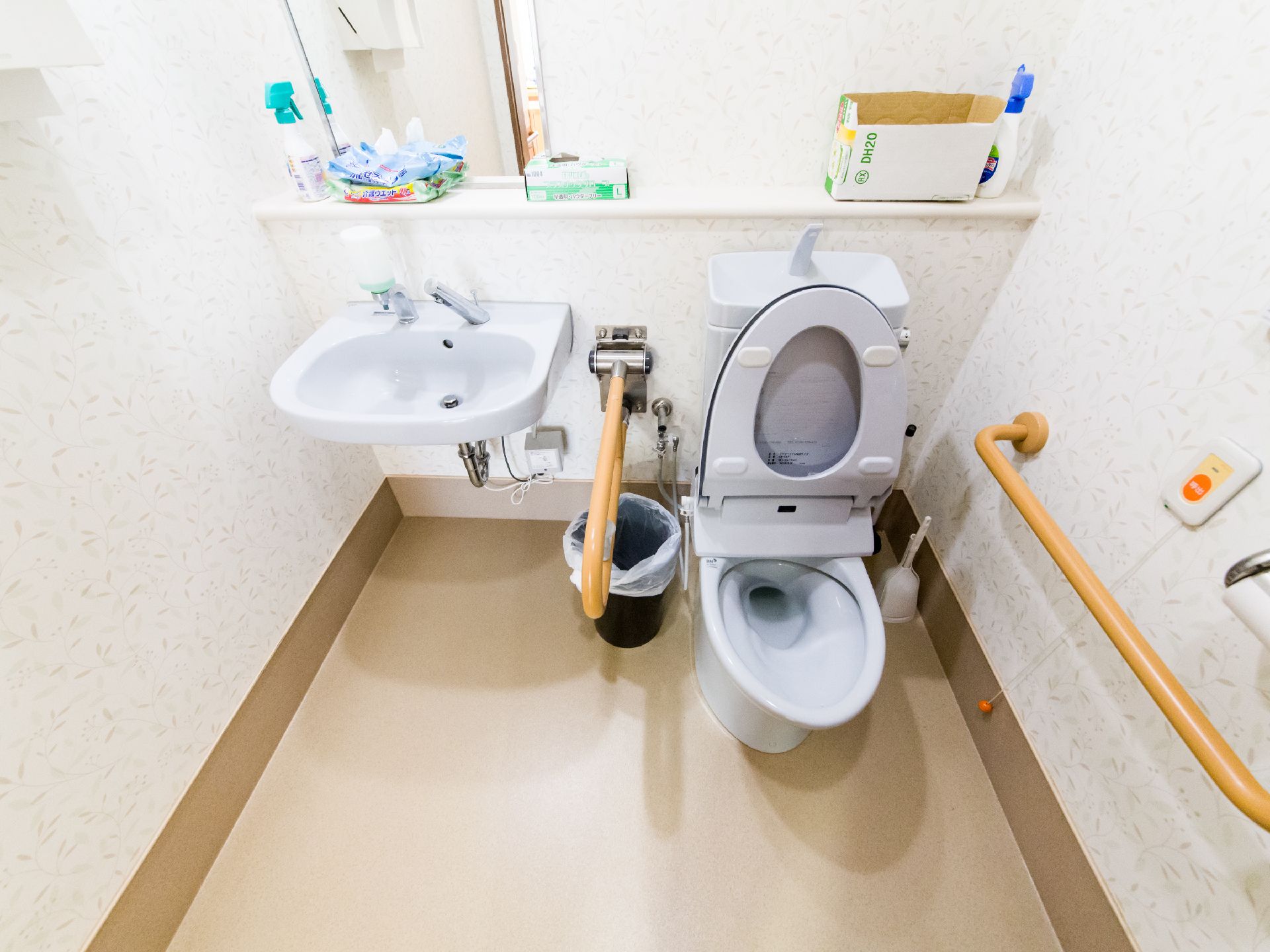 白を基調としたトイレ内は明るい。手洗い場の所には鏡が付いている。掃除用具が置いてある。ナースコールがある。