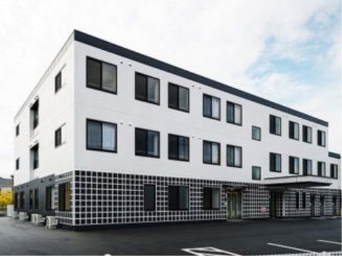 ３階建てのモノトーンな色遣いがおしゃれな建物である。周辺はアスファルトで整地されたバリアフリー仕様である。