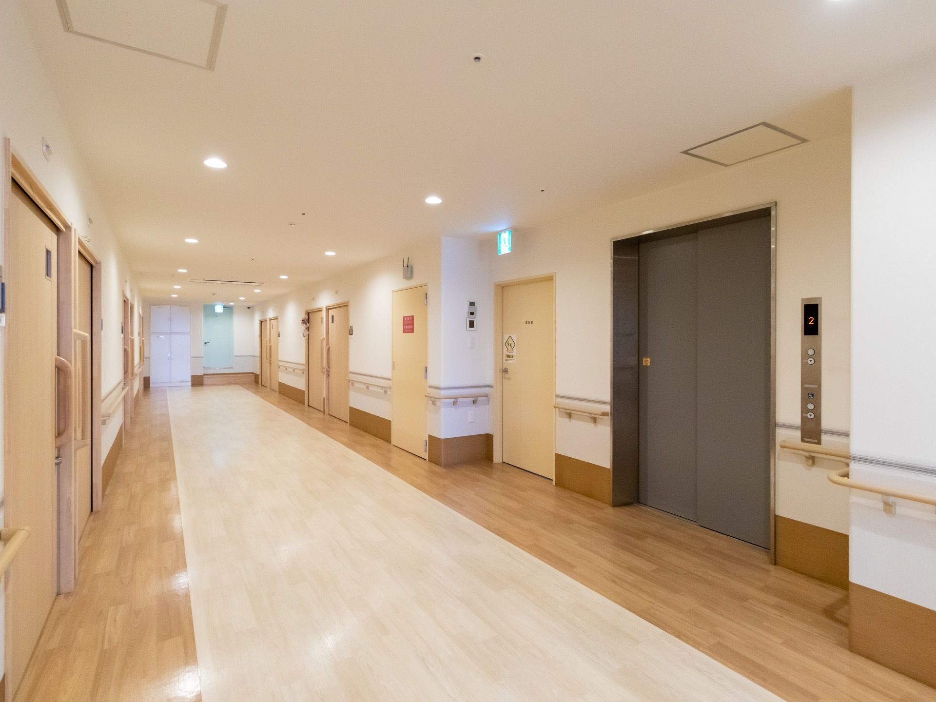 幅の広いフローリングの通路であり、両側の壁面に白木の引き戸が並んでいる。右側にはエレベーターの扉がある。
