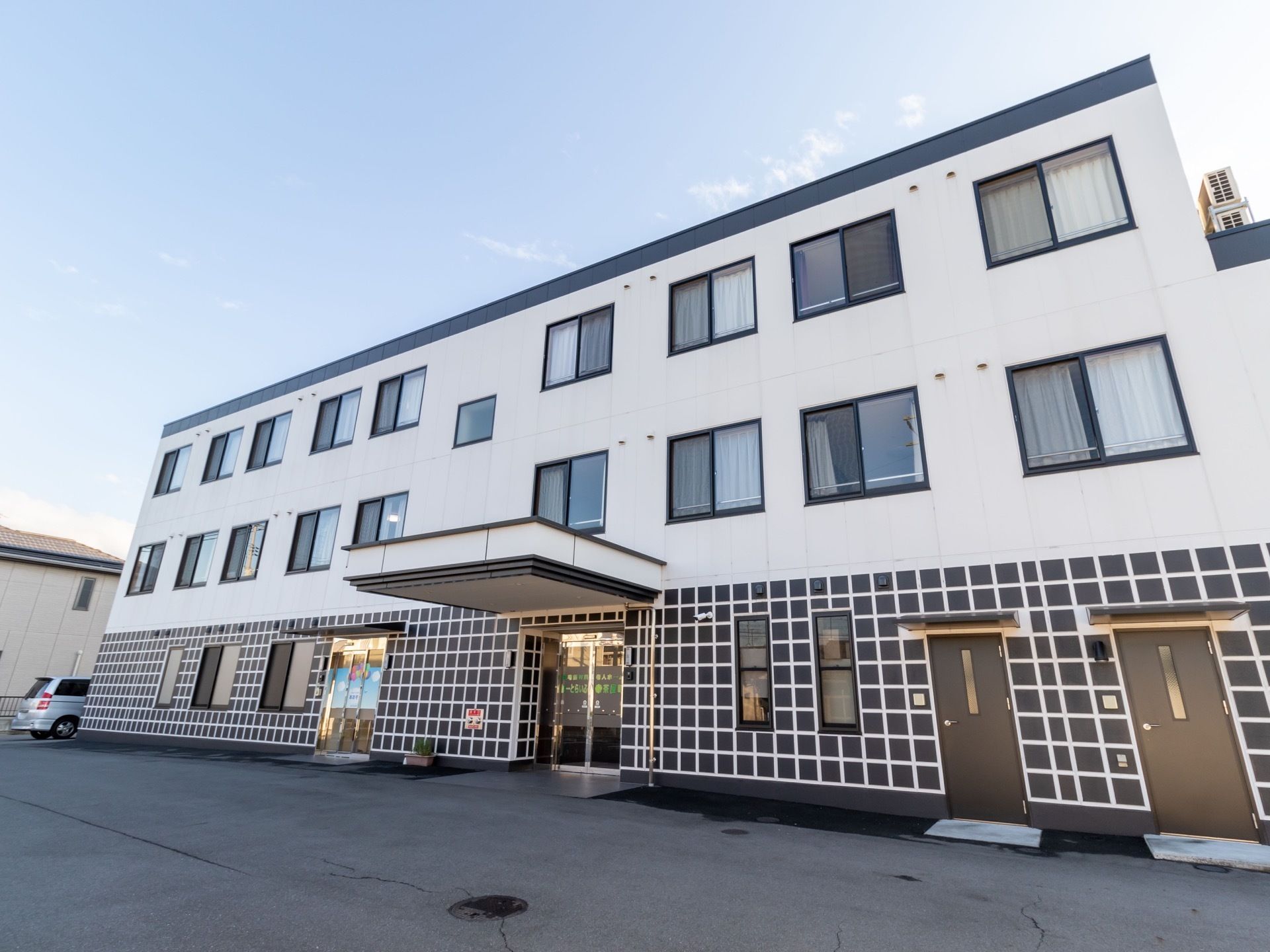 白と黒を基調とした３階建ての施設である。１階部分の外壁には格子状のデザインが施されており、複数の扉や窓が設置されている。