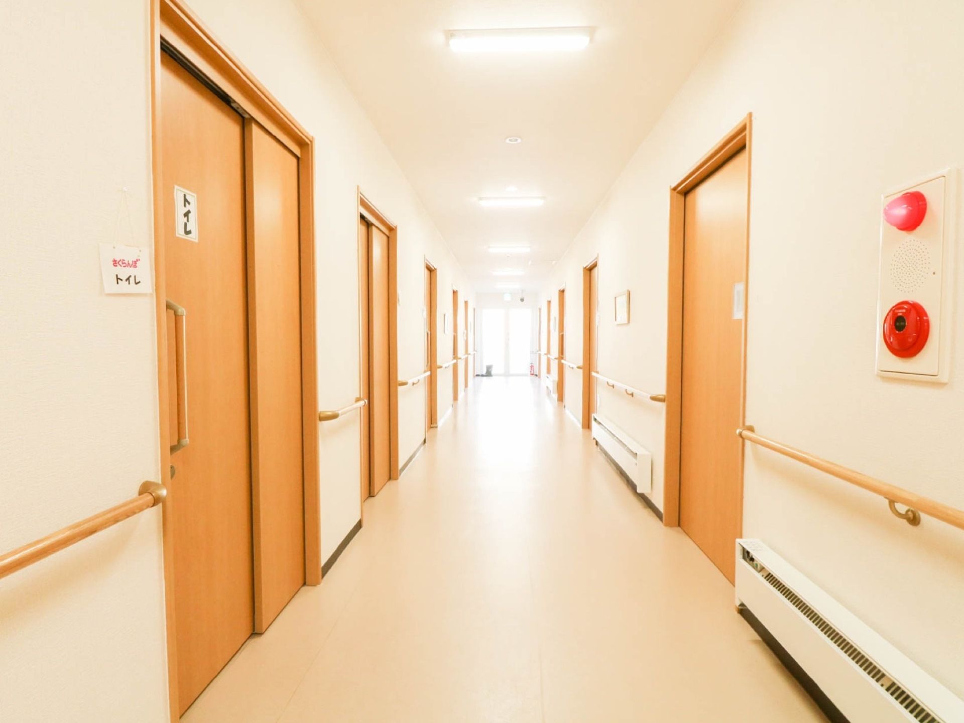 手すりが設置された廊下が伸びている。両側に居室やトイレが並んでいる。足元には空調が付いている。
