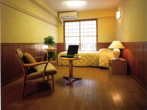 室内は木製の壁やフローリングの床があり、木の温もりを感じることができる。ベッドのそばにはランプや観葉植物が置かれた棚がある。