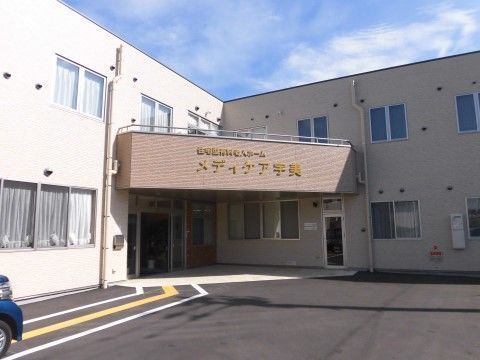 L字型の白い建物の折れの部分にある、ブラウンのひさしの付いた玄関
