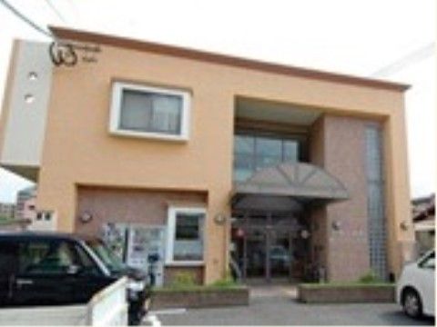茶系の落ち着いた色合いで、デザインも凝っている２階建ての建物。手前には小さな植え込みと駐車場がある。