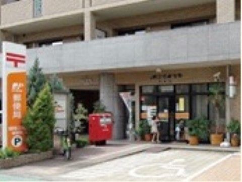 マンションの１階にある郵便局。赤いポストが設置されている。鉢植えがずらりと並び、その前に車椅子専用の駐車場がある。