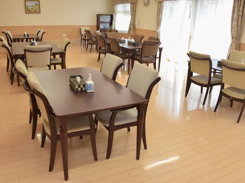 右に窓があり、クリーム色の床にブラウンのテーブルセットが並んだ食堂