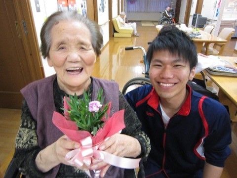 小さな花束を持って喜ぶ高齢女性とその横に寄り添っているスタッフ