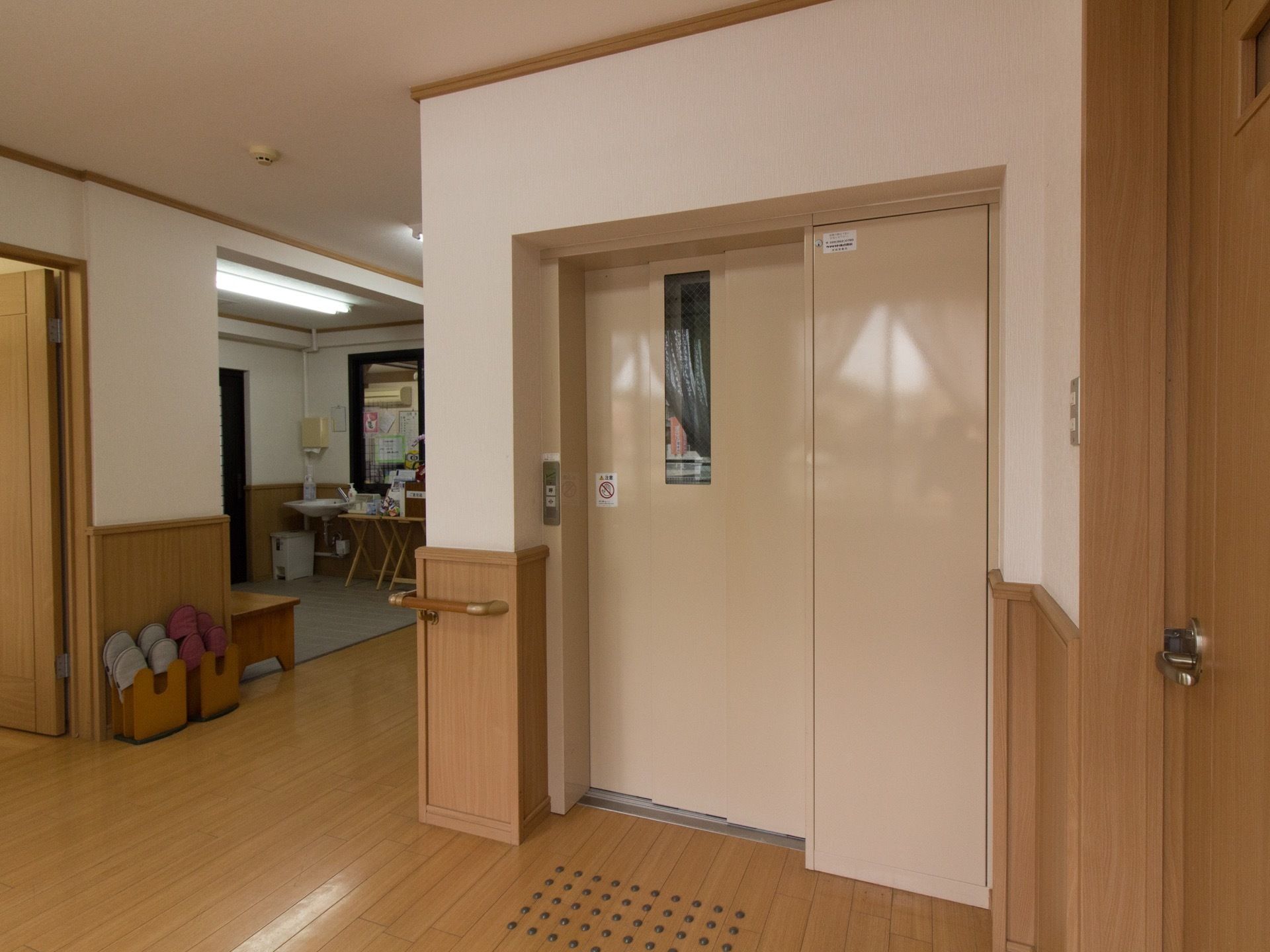 ベージュを基調とした扉のエレベーター。床には点字が設置されており、通路途中に館内履き用のスリッパが用意されている。