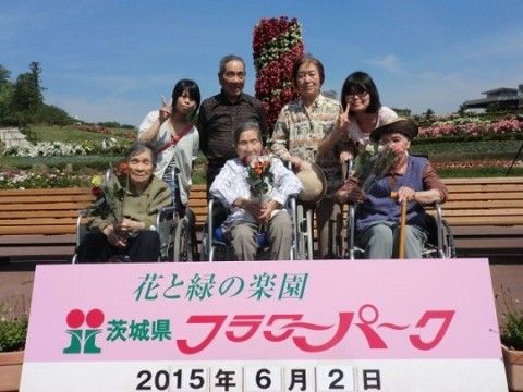 公園の看板の後ろにいる車いすを利用している3人の高齢者とその後ろに立つ4人の人物