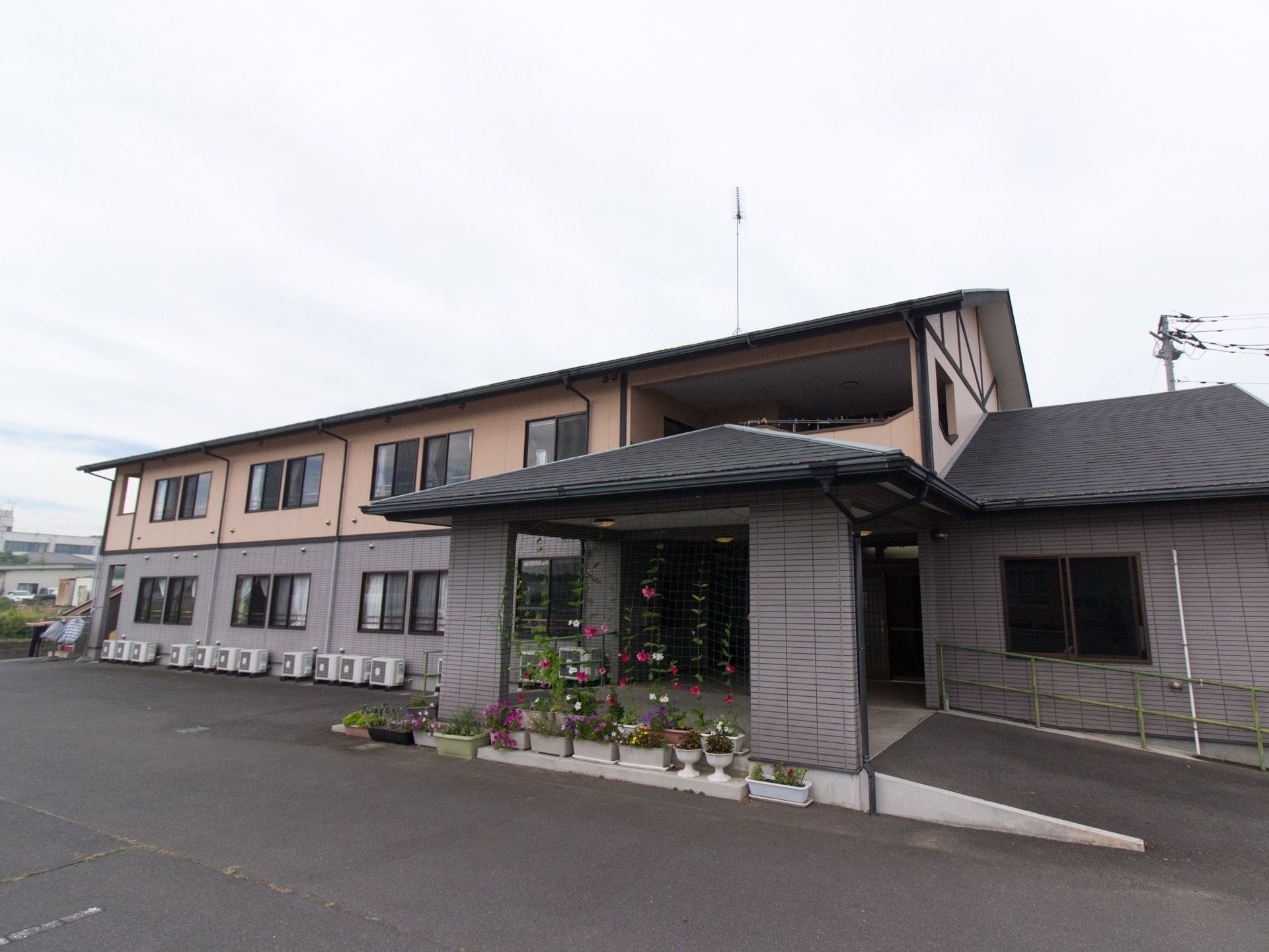 広い敷地に建っている２階建ての施設である。車寄せのある玄関に多くの鉢やプランターがあり、季節の花が咲いている。