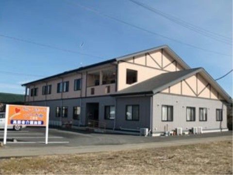 左側に看板が立つ駐車場の奥にある2階建てのツートンカラーの建物