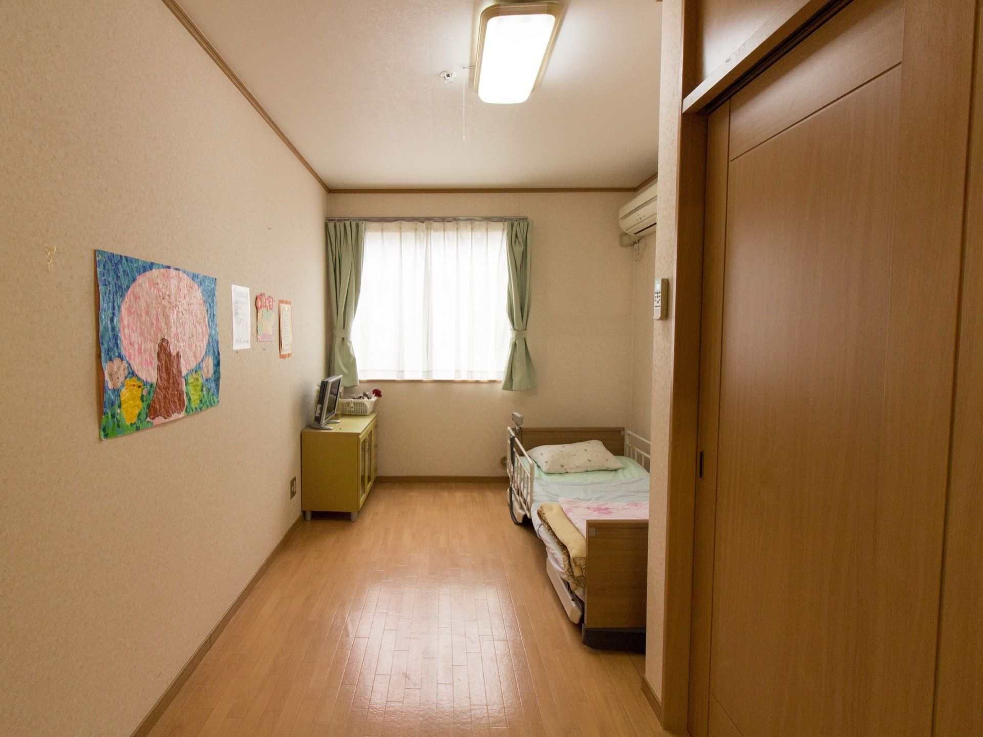 正面に大きな窓がある居室。ベッド横にはテレビや棚があり全体的にゆとりある作りになっている。冷暖房完備で安定した空調管理を実現している。