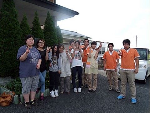 左に建物と植え込みがある場所で、ポーズをとっている10人のスタッフ