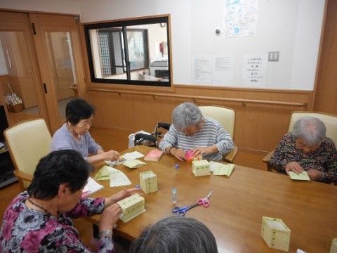 テーブルを囲んで高齢者などが座って作業をしている共用スペース