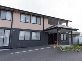 黒と茶色を基調とした現代的な外観の建物。玄関付近にはゆるやかなスロープがあり、手すりも設置されている。