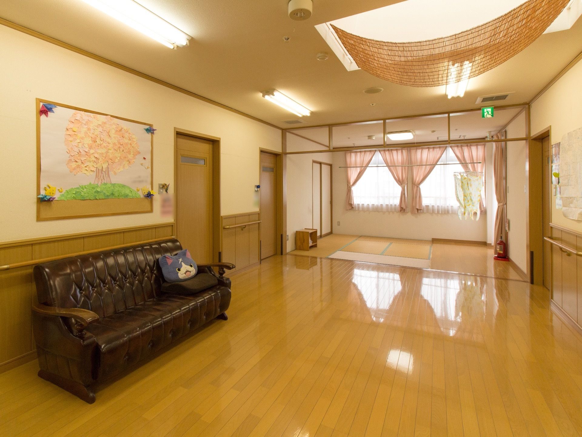 桜の木をモチーフにした手作りのちぎり絵が壁に貼られている。天井にすだれが掛けられ、蛍光灯が設置されている。