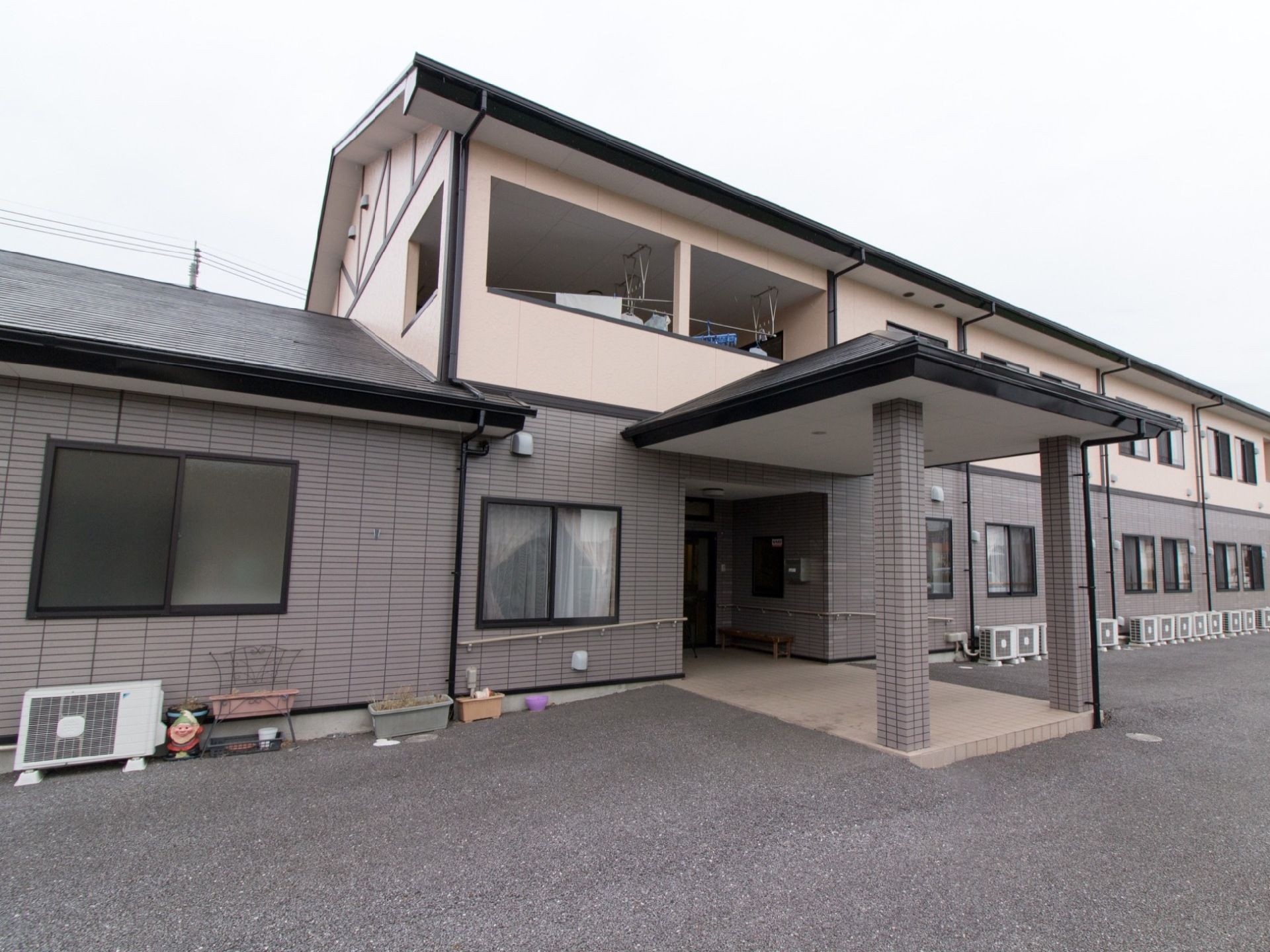 建物は１階がグレーのタイル調と２階が淡いオレンジ色の２トーンカラーの外壁である。建物に沿ってたくさんのエアコンの室外機が置いてある。