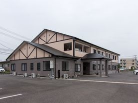 落ち着いた２色使いの外壁が、周囲の景観に良く馴染む２階建ての建物である。建物の周りに駐車スペースを設けている。