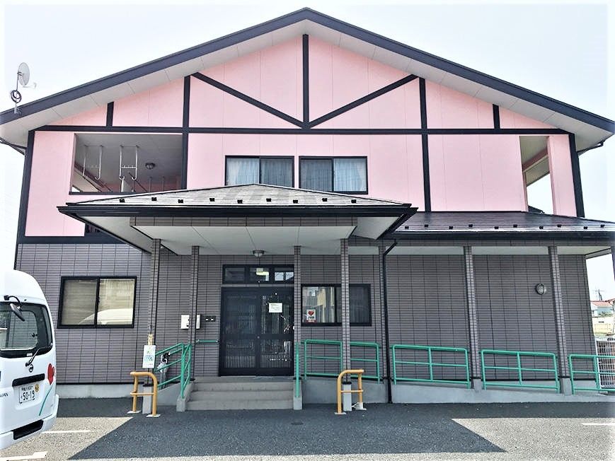 ピンク色の壁に黒いラインが入った壁。屋根は三角形で、2階部分に小さな窓がついている