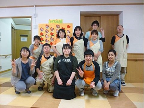 ベージュのタイル張りの床の部屋で、前列5人が屈み、後列6人が立って並ぶスタッフ