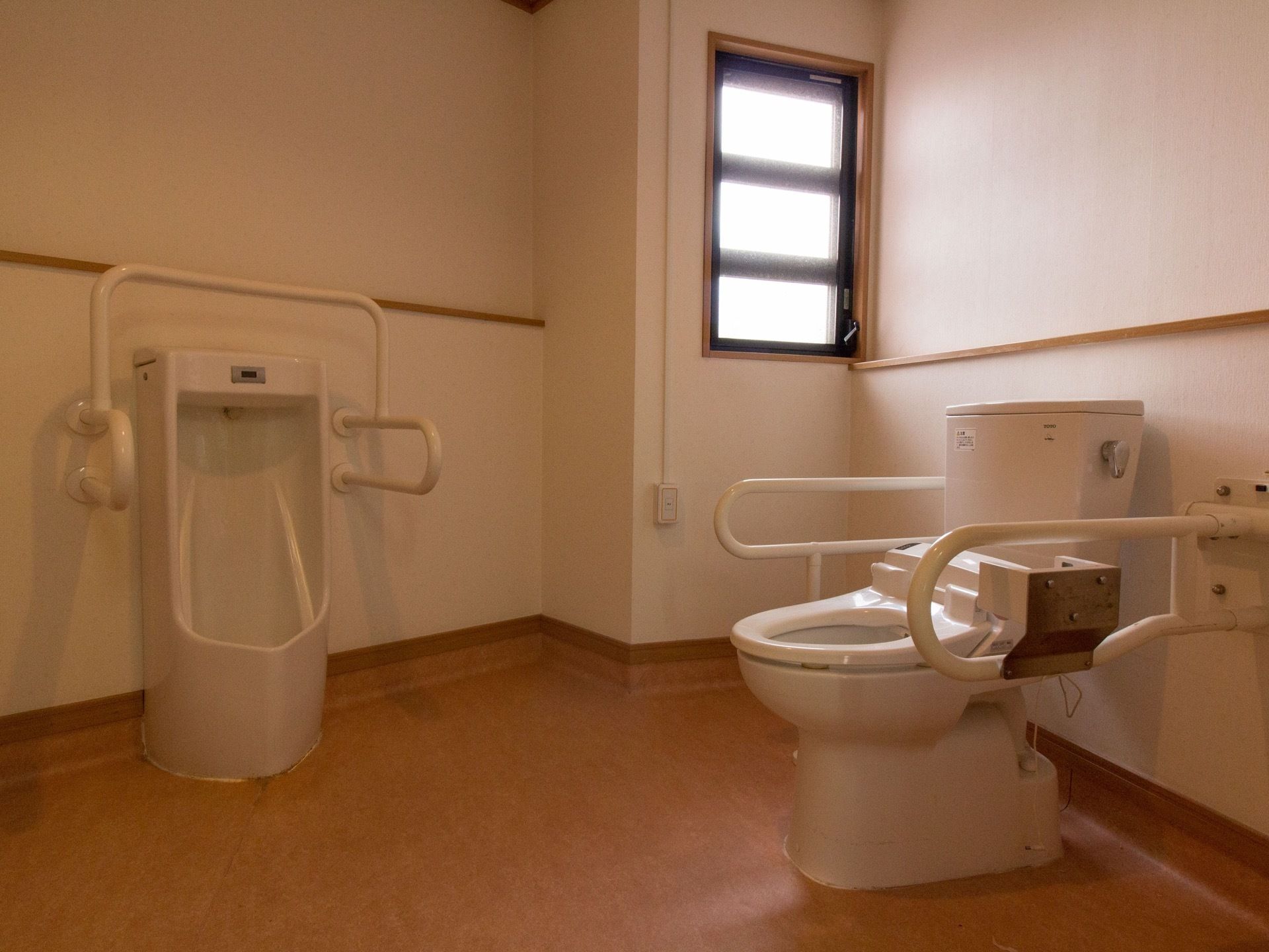 床はフローリングが使用されている。男性用小便器と洋式便座の2種類が用意されている。壁に窓が設置されている。