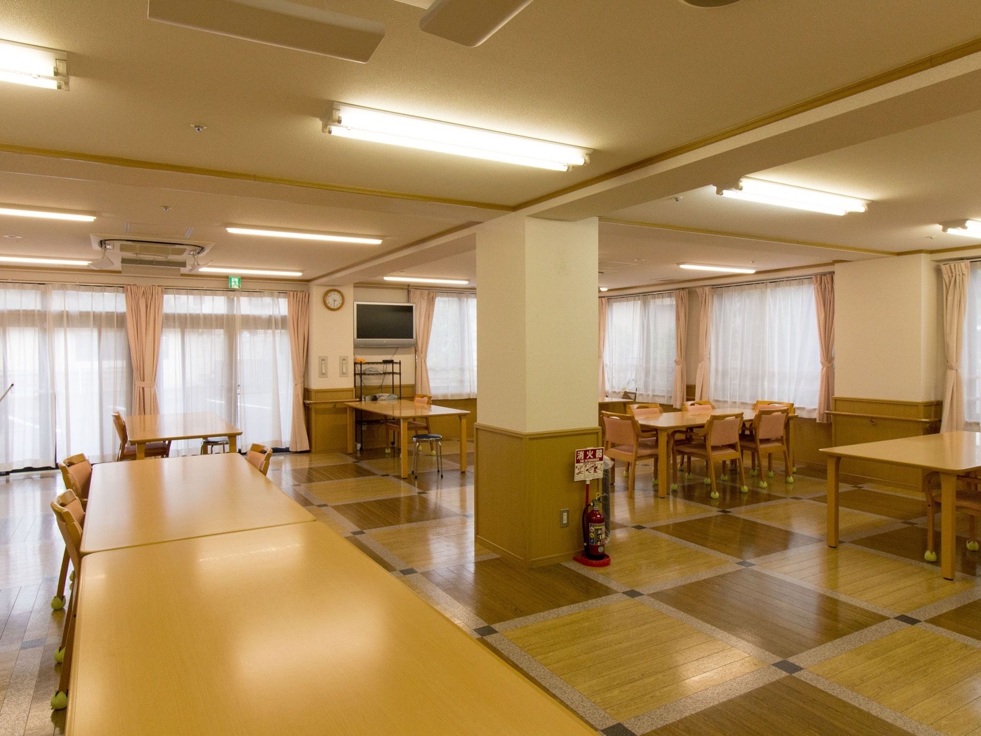 机が数卓と椅子数十脚が広々としたスペースに置かれている。大きめのテレビが壁の高い位置に設置されており、どの場所からもご覧いただける。