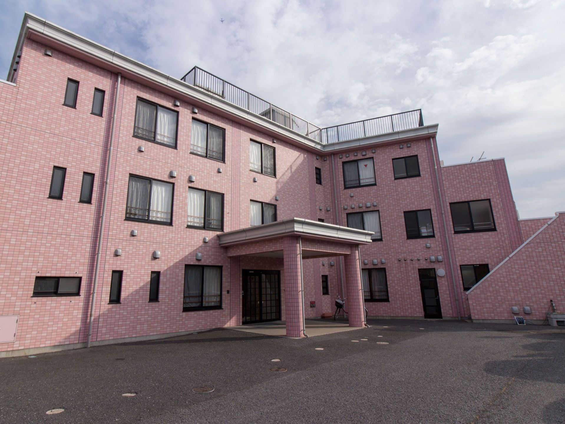 建物は明るく落ち着いた色合い。玄関には大きなひさしがある。玄関前はきれいに舗装された広いスペースがある。