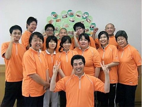掲示物のある壁の前で、先頭に1人、あとは6人ずつ2列に並ぶスタッフ