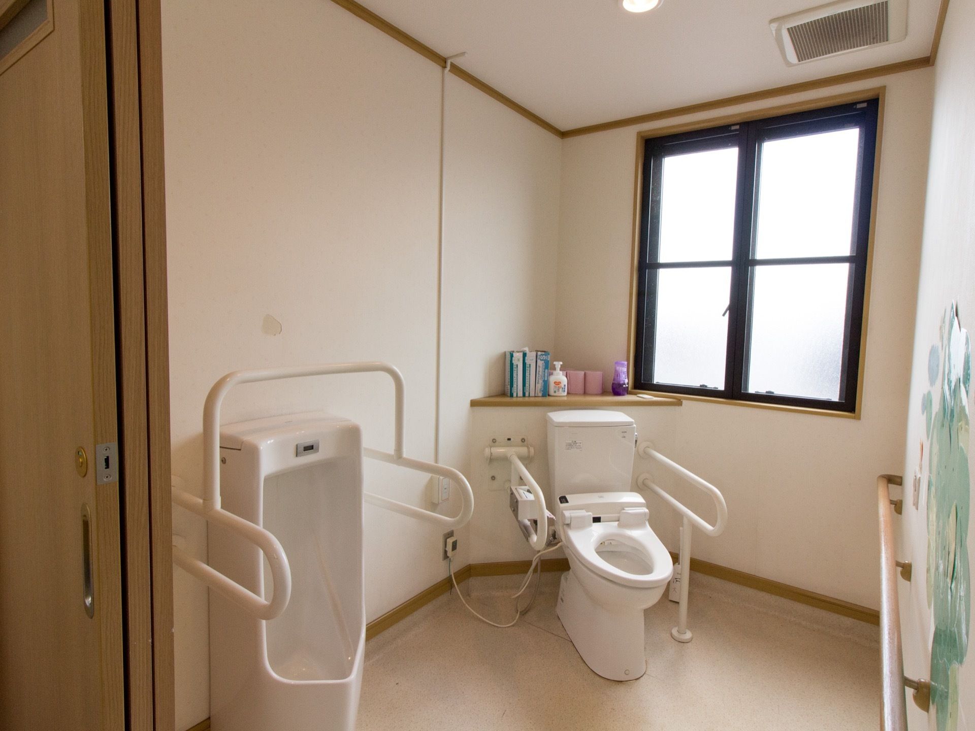 明るく清潔感のあるトイレである。手前側の小便器には樹脂製の手すりが廻されており、万一の転倒を防止している。