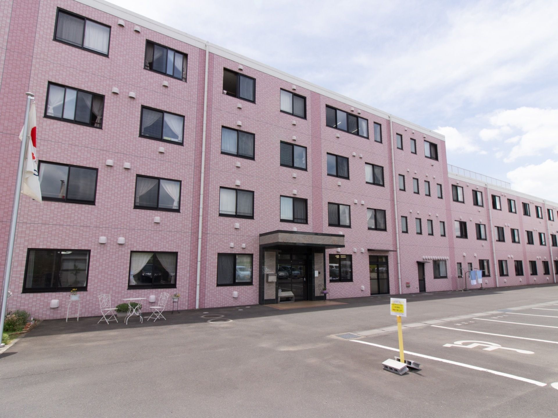 明るく落ち着いた印象のピンク色の建物である。３階建てと４階建ての部分があり、駐車場からのアクセスもよい。