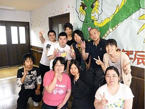 大きな竜のイラストが掲示された壁の前で前列4人、後列6人で並ぶスタッフ
