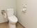 トイレの壁に温水洗浄便座を操作するパネルが取り付けられている。便座の横には折り畳み式の手すりが設置されている。