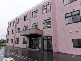 建物は壁がピンクのタイルが一面に貼られている。玄関前には屋根がせり出し、入口横にポストが設置されている。