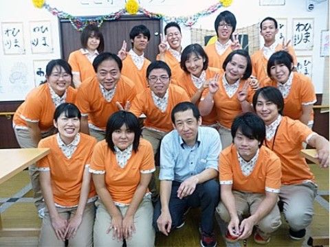 習字の作品や飾り付けが貼られた壁の前で3列になって並んでいるスタッフ