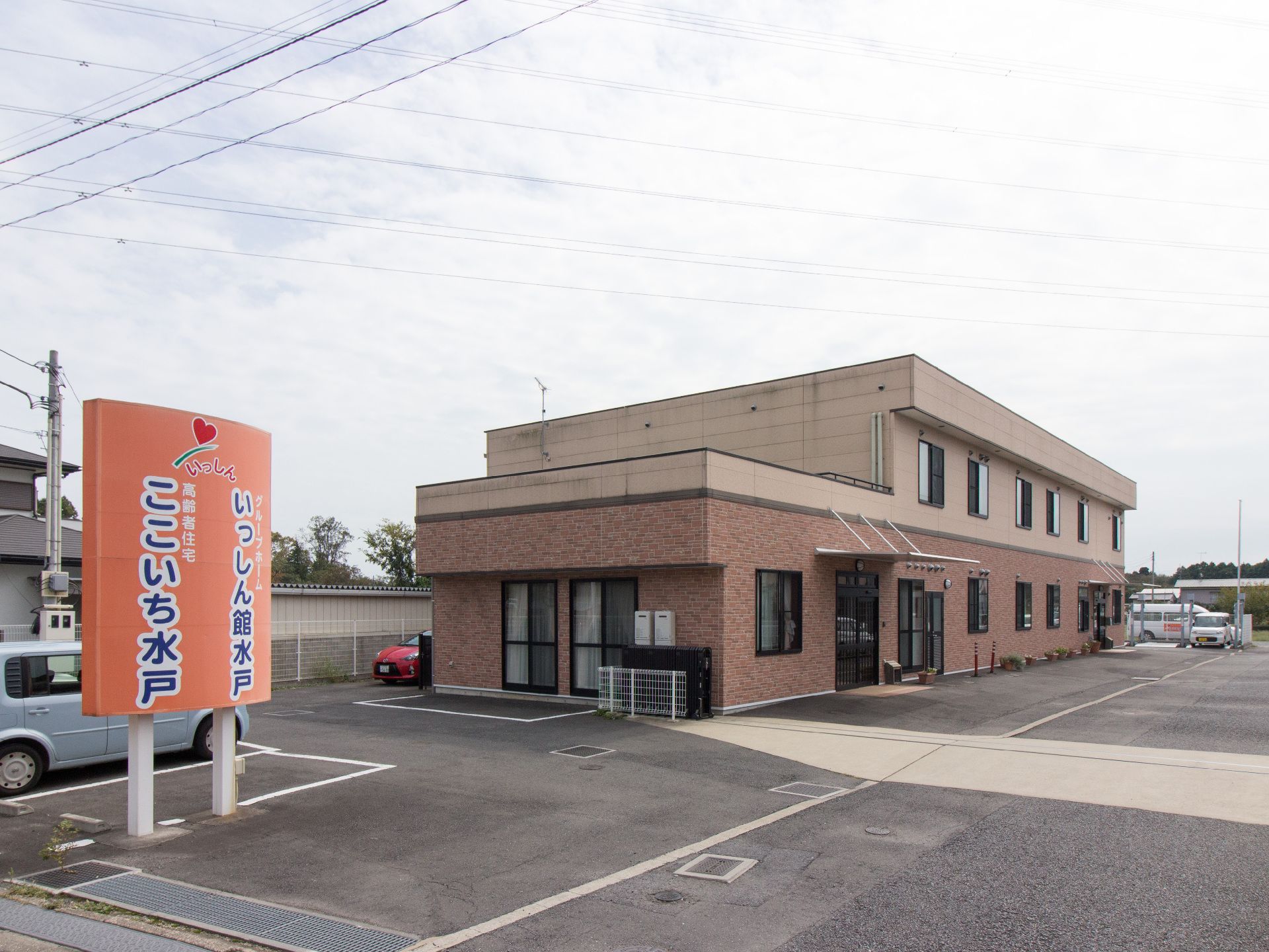左にオレンジの看板が立つ駐車場の向こうにあるツートンカラーの2階建ての建物
