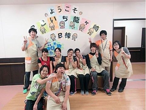 歓迎の意味の掲示が貼られた壁の前で、ピースサインなどをする10人のスタッフ