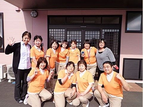 ピンクの壁、格子の入ったガラスの引き戸の玄関の前で2列に並ぶスタッフ