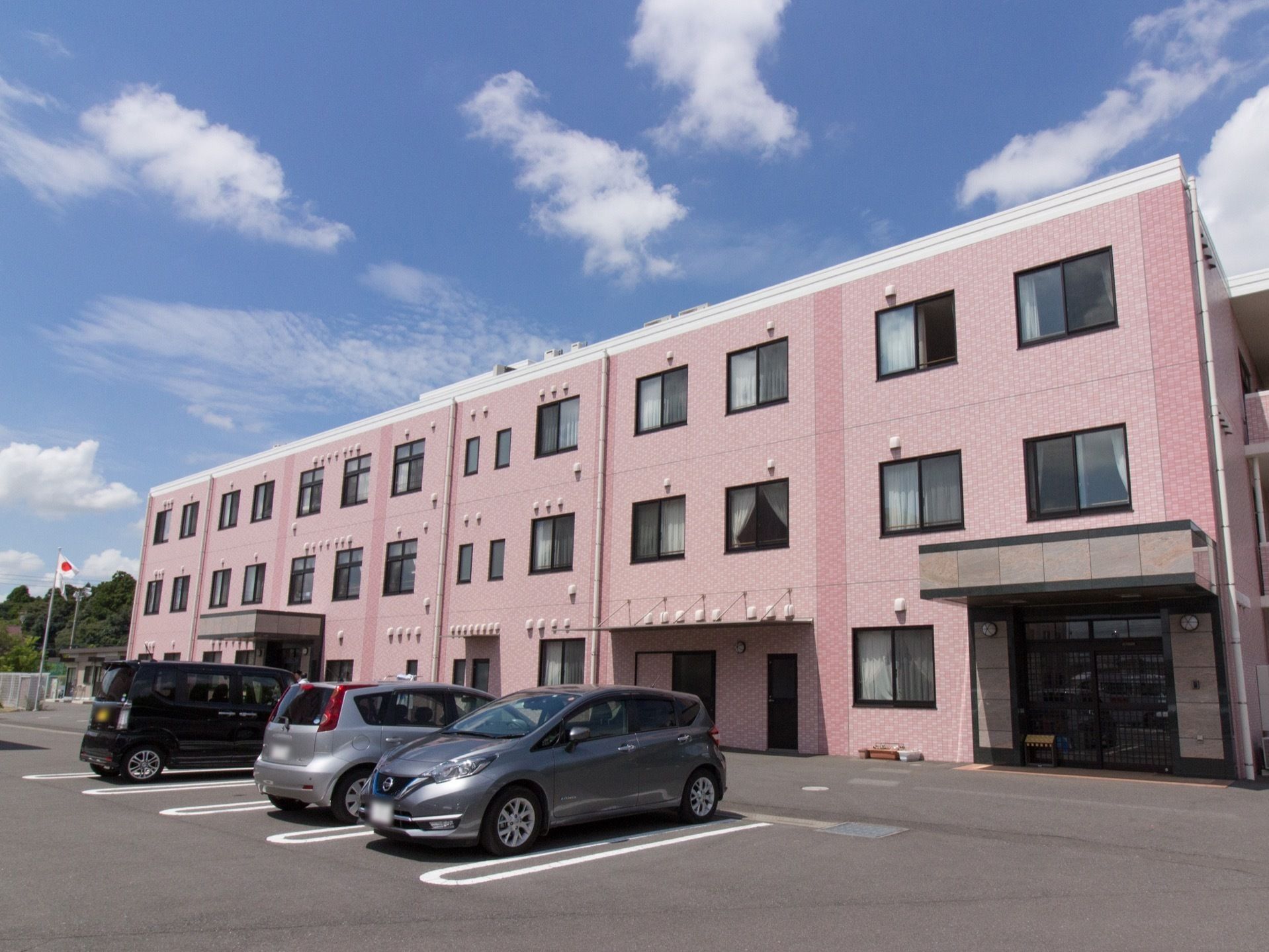 ピンク色の３階建の建物である。駐車場から玄関に到るまで段差はなく、緩やかなスロープになっている。出入り口が２箇所についている。