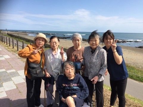 水辺にある手すりの付いた遊歩道のような場所に、車椅子の女性を囲んで立つ5人の女性