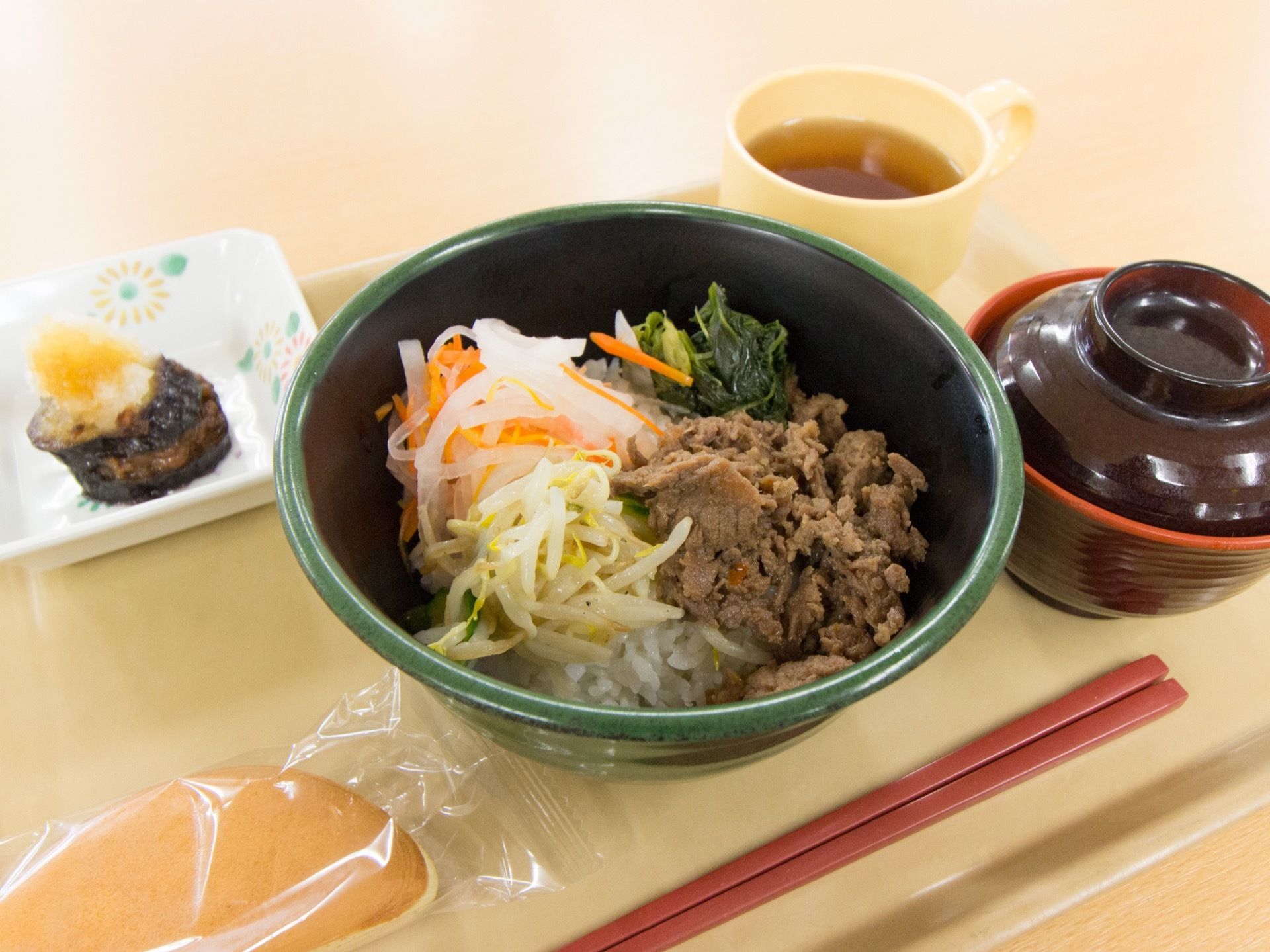 ベージュのお盆に、料理がバランスよくならべられている。この日のメニューはどんぶりがメイン。おやつもついている。