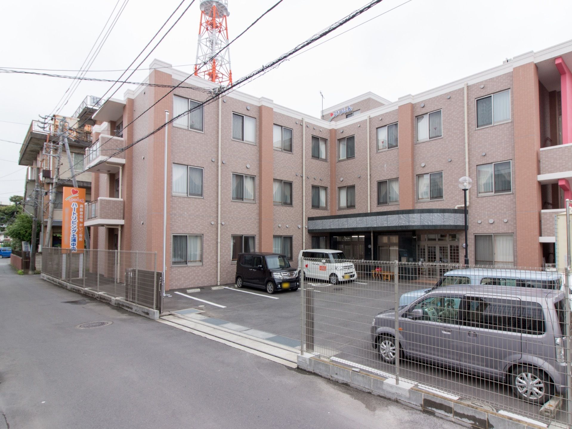 道路から見た施設。建物は３階建て構造になっており、ちょうど曲がったところに横に広い玄関が配置されている。