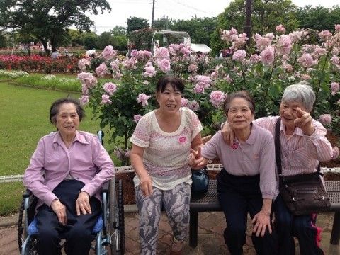 ピンクの花が咲く前で車椅子に座った高齢女性と、その右のベンチに腰掛ける3人の女性