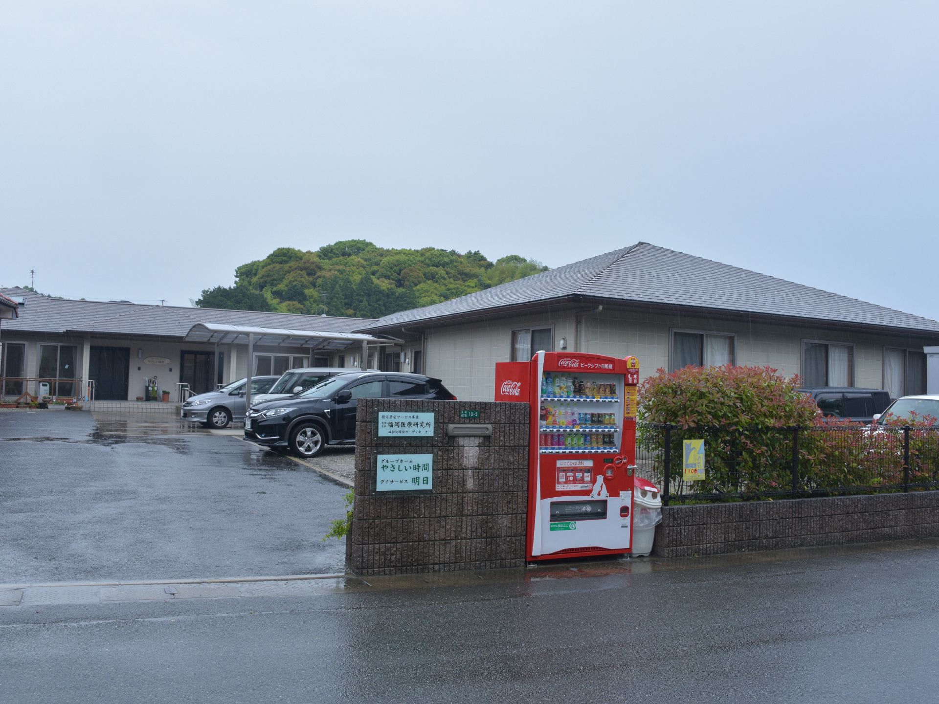 郵便受けの付いた石の門に施設名の看板がある。門を入ると駐車スペースがありその奥に施設が建っている。施設は1階建てである。