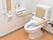 オレンジ色の床のトイレである。壁には縦型の手すりが取り付けられている。また、便座にもクッション付きの手すりが取り付けられている。