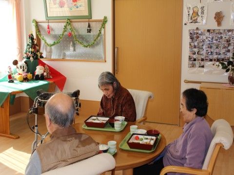 テーブルに並べられたお弁当を前に、椅子に腰かけている3人の高齢者