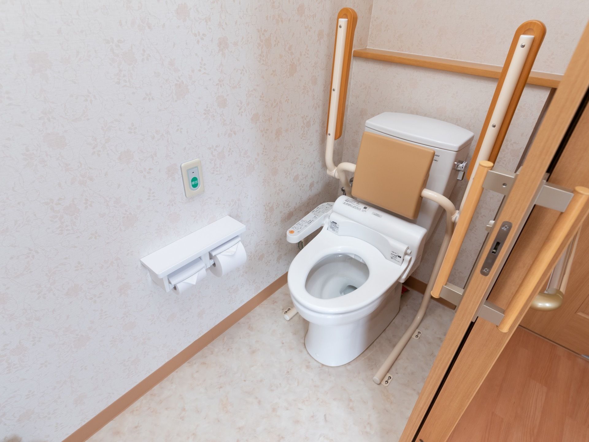トイレのドアはスライド式で開閉がしやすい。便器の両側には可動式の手すりが、タンクの近くには背もたれが取り付けられている。