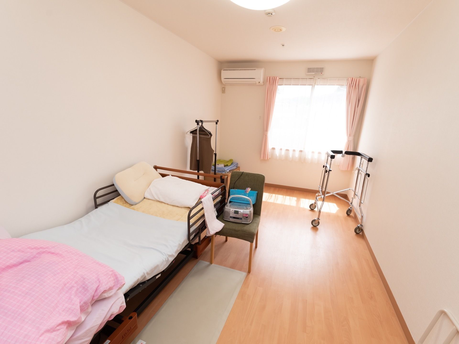 居室には転落防止の柵が付いた介護用ベッドが備え付けられている。奥行きがある部屋で、ベッドと窓の間にパイプハンガーなどを置くことができる。
